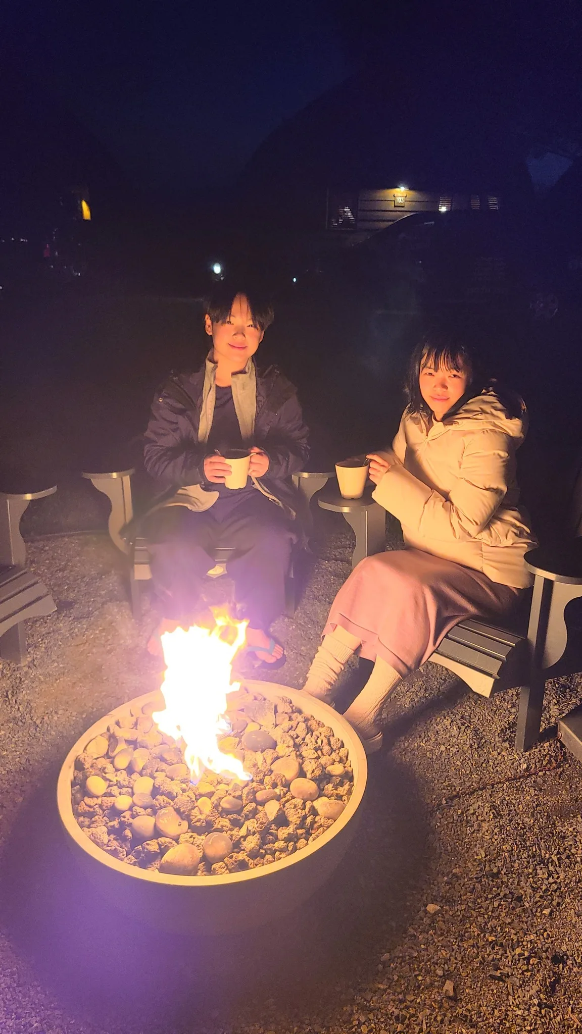 家人在夜晚戶外營火旁拿著熱飲
